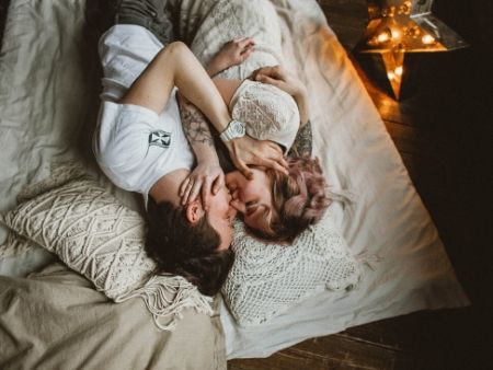 oblečený muž aj žena ležia v posteli a chytajú si navzájom tvár