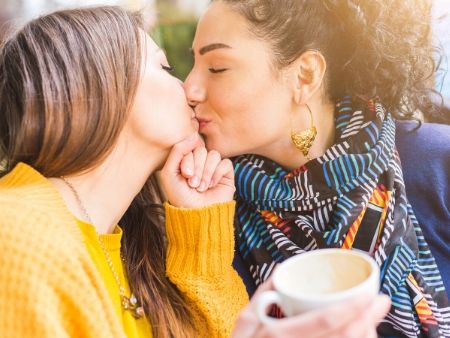 dve ženy držia kávu a bozkávajú sa na ústa