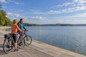 Dvojica s bicyklami na námestovskom nábreží pri Oravskej priehrade, ilustračná AI fotografia