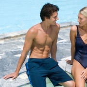 blondína a muž sedia na okraji bazéna a usmievajú sa na seba