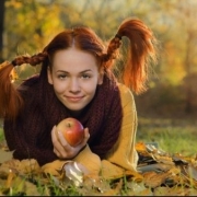 žena s ryšavými vrkočmi a jablkom v ruke leží na lístí v záhrade