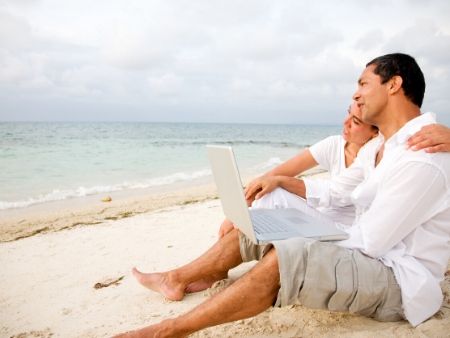dvojica sedí na pláži, pozerajú na more a muž má na kolenách notebook