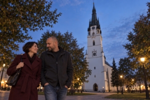 Dvojica pri kostole Nanebovzatia Panny Márie v Spišskej Novej Vsi za súmraku, ilustračná AI fotografia
