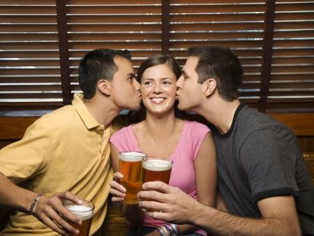 dvaja muži bozkávajú ženu a všetci držia v ruke pohár piva