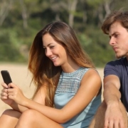 muž pozerá cez plece žene do mobilu žiarlivo